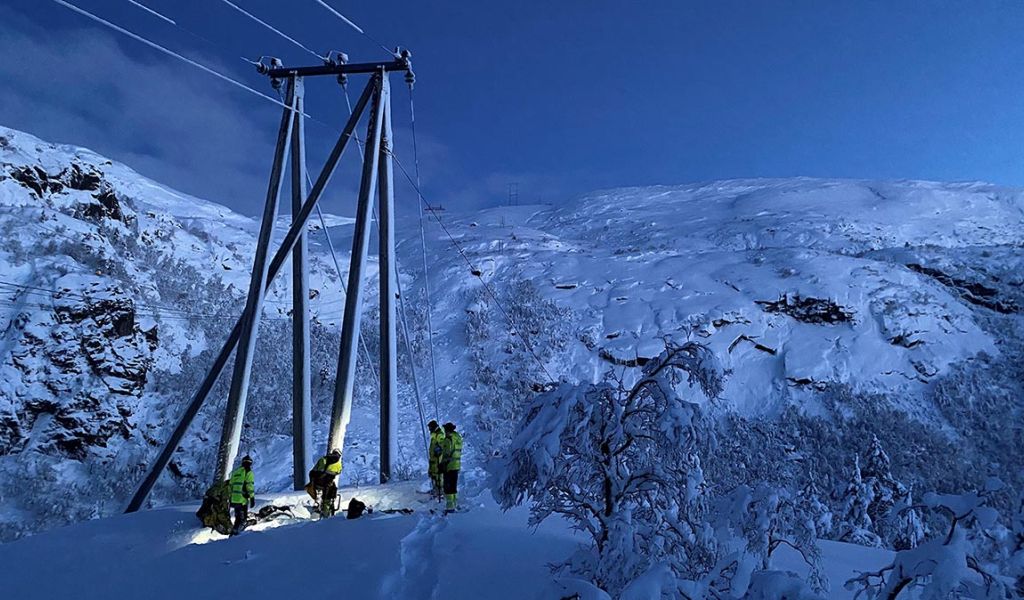 i skumringen: energimontører i arbeid ved strømmast i et snøbelagt område med trær og fjell
