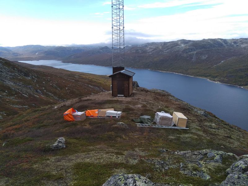 oppføring av telemast og hytte på fjellet med fjord i bakgrunn