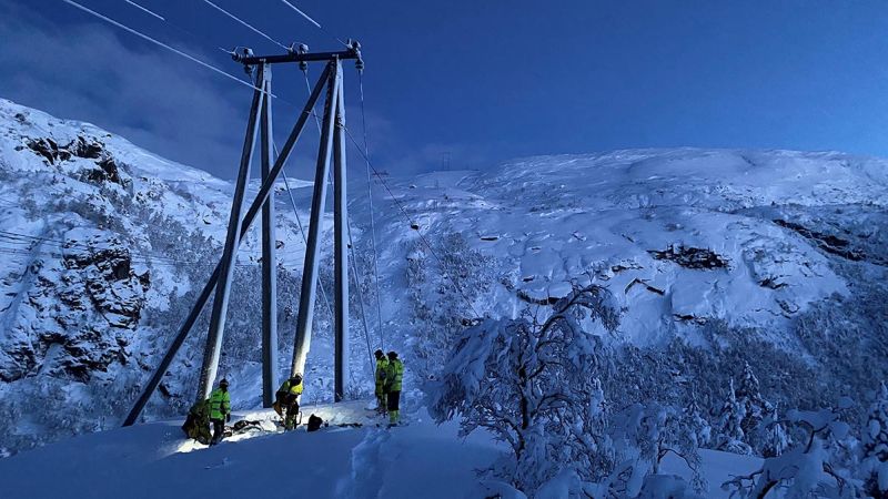 i skumringen: energimontører i arbeid ved strømmast i et snøbelagt område med trær og fjell