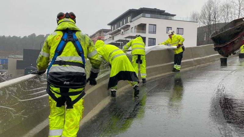 arbeidere dekker til nystøpt betongrekkverk med plast i regnværet