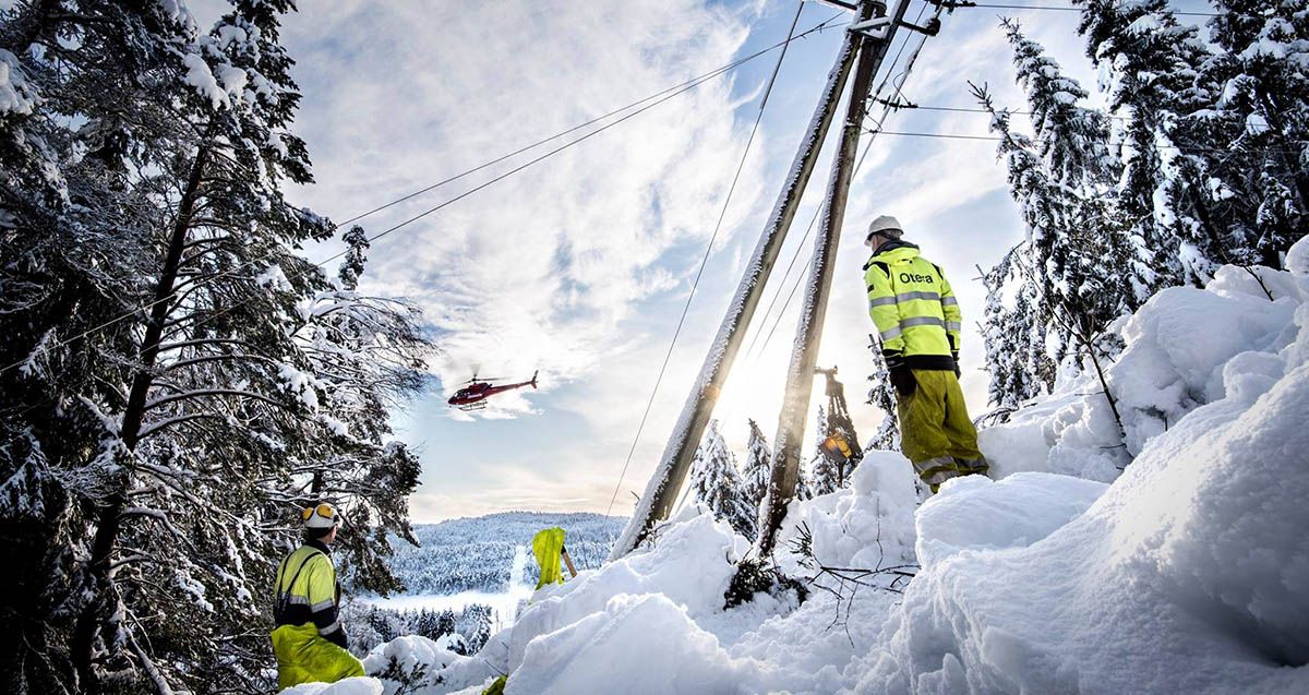 energimontører i vinterlandskap ved skjev mast i skogen og ser på et helikopter