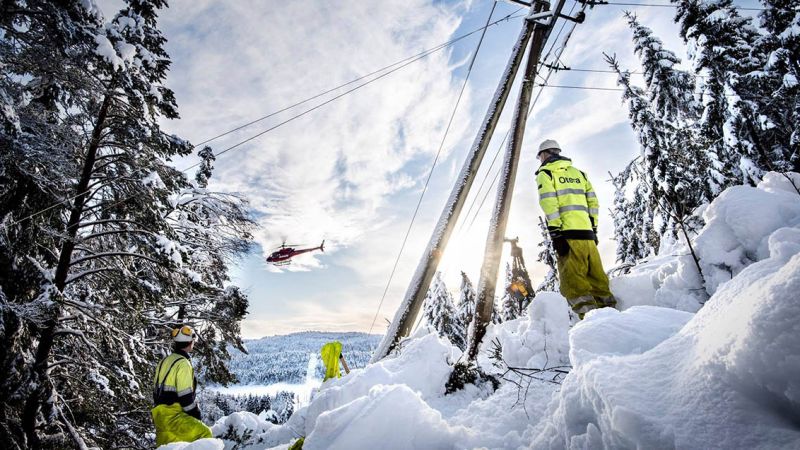 energimontører i vinterlandskap ved skjev mast i skogen og ser på et helikopter
