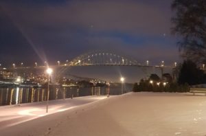 kveldsbilde av snølagt terreng langs elv med bro med veilys i bakgrunnen